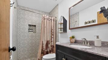 A bathroom with a shower, toilet, sink, and a mirror.