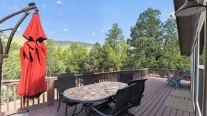 A deck with a round table and chairs, a red umbrella, and a view of trees and hills. - Pine Cabin w View, Fireplace, Deck & Game Room (Pine)