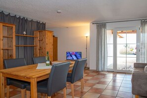 Ein Essbereich mit einem Holztisch und Stühlen, einem Fernseher und Blick durch eine Glastür.