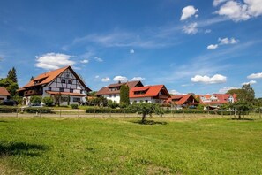 Eine Reihe traditioneller Häuser mit roten Dächern und weißen Wänden, eingebettet in ein grünes Feld unter blauem Himmel.
