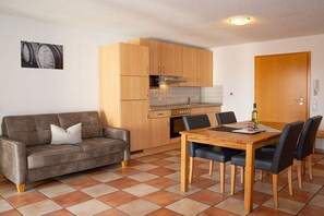 A compact living space with a kitchenette, a dining area with a wooden table and chairs, and a sofa with a cushion. - Holiday apartment with 1 bedroom (Meersburg)