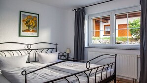 A bed with a metal frame, a bedside table with a lamp, a window with curtains, and a framed picture on the wall. - Holiday apartment with 1 bedroom (Meersburg)