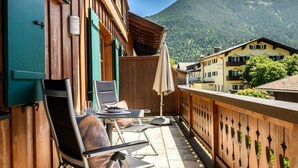 Ein Balkon mit Sitzgelegenheit, Blick auf die Berge und traditioneller Holzarchitektur.