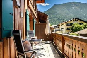 Een balkon met buitenmeubilair, een uitzicht op de bergen en traditionele houten architectuur.
