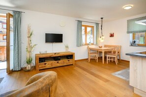 A living room with a wooden TV stand, a dining table with chairs, and a kitchen area with a counter. - Holiday apartment with 1 bedroom (Farchant)
