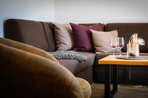 Un canapé marron agrémenté de plusieurs coussins, une table d’appoint en bois avec deux verres à vin et un vase décoratif, ainsi qu’un plaid à motifs léopard.
