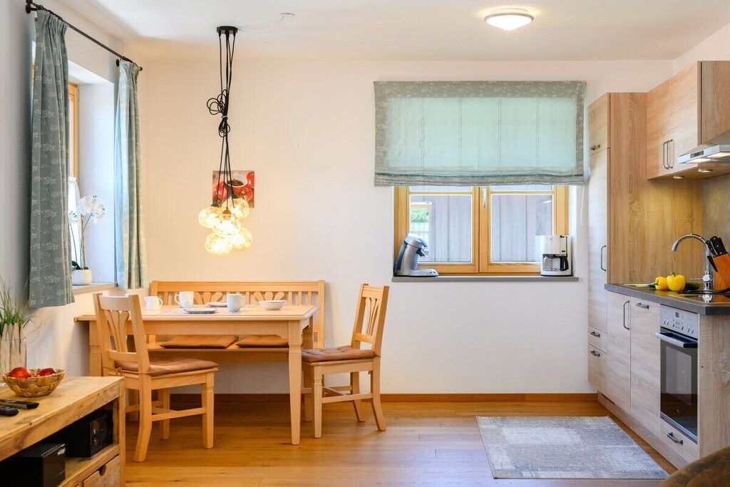 Una cocina compacta con una mesa de comedor, sillas, una lámpara colgante, un ventanal con vistas y armarios de madera.