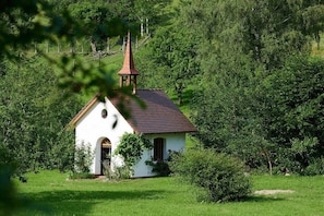 Eine kleine weiße Kirche mit rotem Dach und einem Glockenturm, umgeben von üppiger Vegetation.