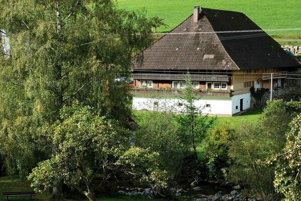 Een klassiek chalet met schuin dak, omgeven door weelderige begroeiing en een stenen muur.