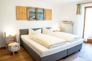 Ein Schlafzimmer mit einem Bett, einem Holzschrank mit einem Bild, einem Heizkörper und einem Fenster mit Vorhängen.