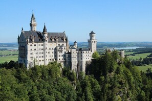 A large, historic castle with multiple towers and a prominent central building, surrounded by dense forest. - Tegelberg in the Geiger country house (Füssen)