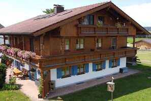Ein zweistöckiges Holzhaus mit Balkon, überdachter Veranda und einem kleinen Garten.