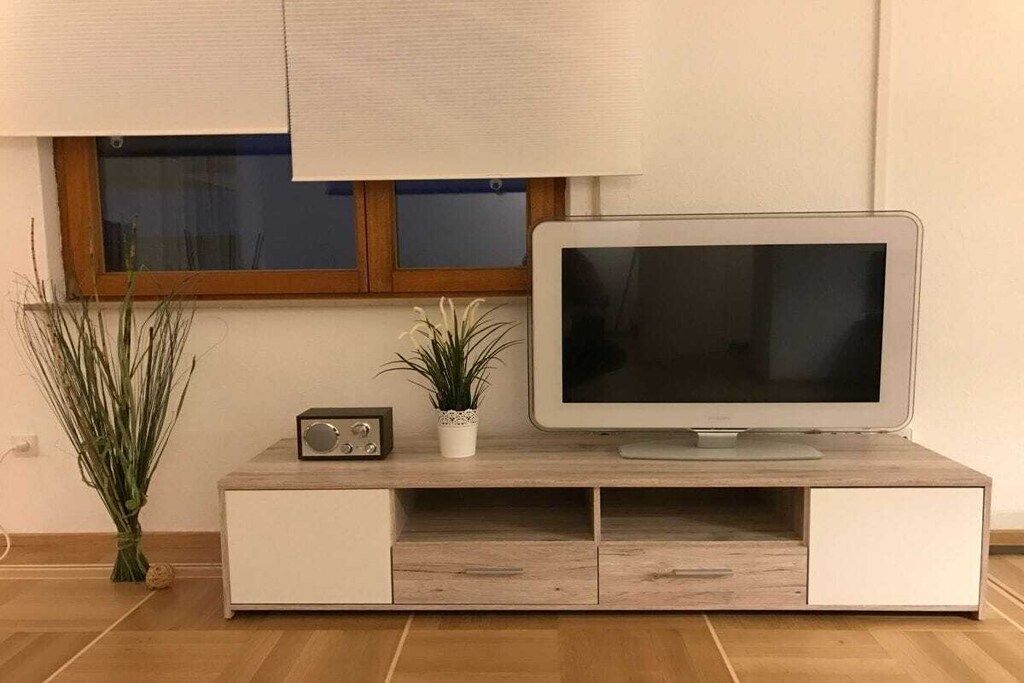 Un televisore a schermo piatto su un mobile in legno, con una pianta e una radio.
