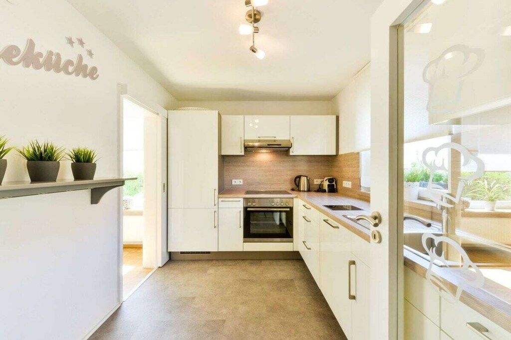 Een moderne keuken met witte kasten, een ingebouwde oven en een aanrecht met een waterkoker.
