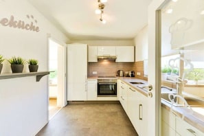 A modern kitchen with white cabinetry, a built-in oven, and a countertop with a kettle.