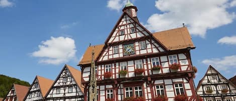 A traditional half-timbered building with a clock, windows with flower boxes, and a visible church steeple.
