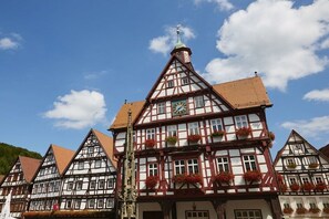 A traditional half-timbered building with a clock, windows with flower boxes, and a visible church steeple. - Four Seasons || Bad Urach (Bad Urach)