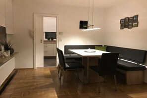 A modern dining area with a white table, black chairs, and a bench. There is a kitchen visible through an open door. - Four Seasons || Bad Urach (Bad Urach)