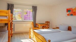 A room with a bunk bed, a single bed, a table with chairs, a radiator, and a window with curtains. - Holiday apartment with 1 bedroom (Meersburg)
