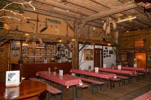 Ein Restaurantinneres mit Holzbalken, rot-weiß karierten Tischen und einer Bar mit Regalen voller Flaschen.