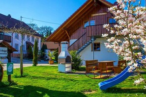 Ein Holzgebäude mit Rutsche, Grillplatz und einer Bank.
