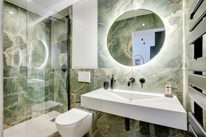 A modern bathroom with a glass-enclosed shower, a white sink, and a marble wall. - Résidence Laffitte (Paris)