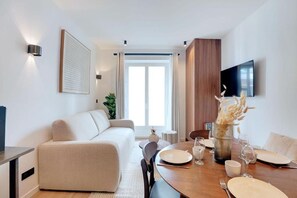 A modern living room with a sofa, dining table set for four, and a flat-screen TV mounted on the wall. - Résidence Laffitte (Paris)