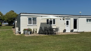 A single-story mobile home with a patio area, a table and chairs, and potted plants. - Property (Rye)