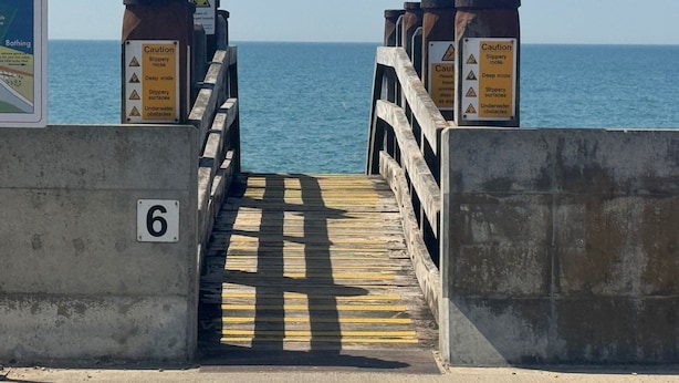 A wooden pier leading to a body of water with caution signs warning of slippery rocks and underwater obstacles. - Property (Rye)