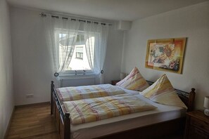 A bedroom with two beds, a window with sheer curtains, a radiator, and a wall-mounted painting. - Holiday apartment with 2 bedrooms (Bernkastel-Kues (Andel))