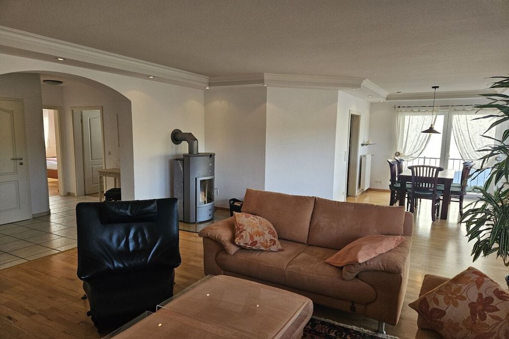 Een woonkamer met een bank, een salontafel, een open haard en een eethoek met een tafel en stoelen.