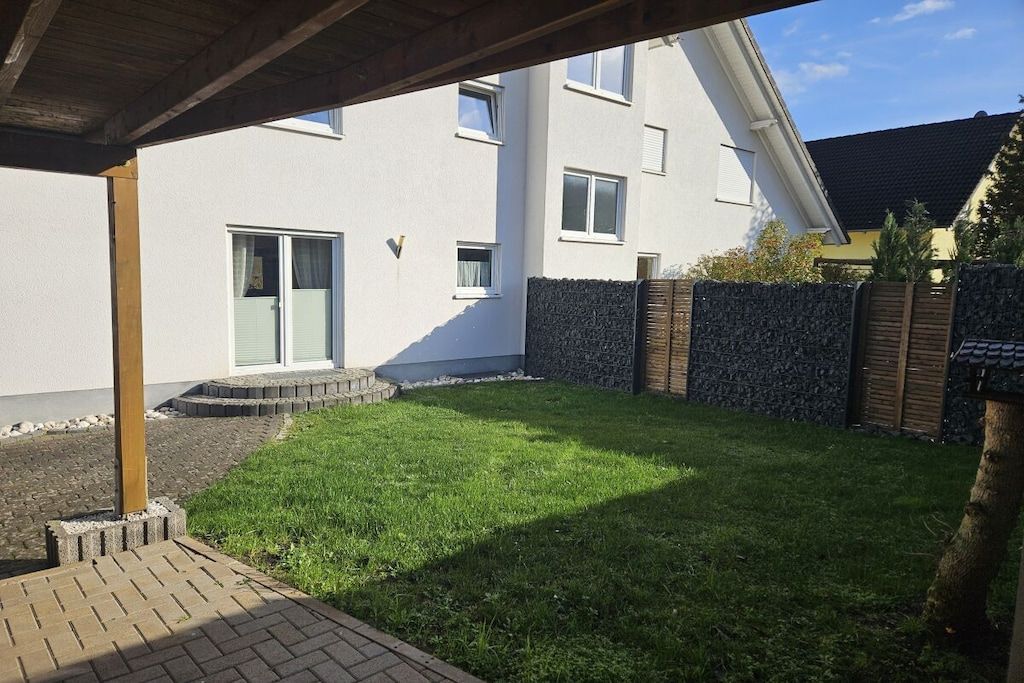 Un immeuble résidentiel doté d’une terrasse pavée, d’un mur en pierre et d’une cour gazonnée.