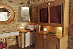 Eine kleine Küche mit Steinwand, Spüle, Geschirrspüler, Holz Arbeitsplatte und einem Schrank mit Tür in rotem Muster.