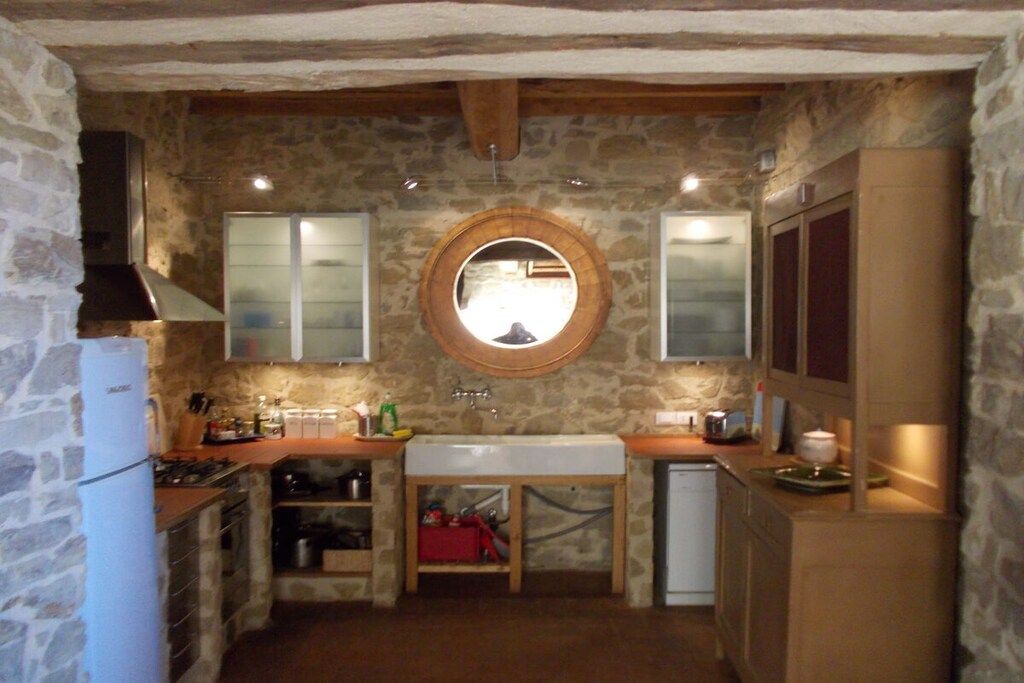 Une cuisine de taille réduite avec un mur en pierre, un miroir rond et des appareils électroménagers de base.