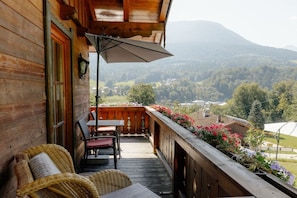 A wooden balcony with wicker furniture, a table, and chairs, overlooking a mountainous landscape. - Stefanie Holiday Apartments (Berchtesgden)
