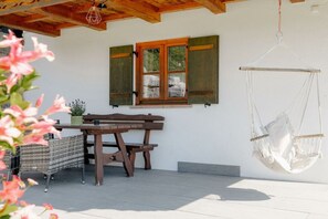 A wooden table and bench set against a white wall with a window and a hanging hammock. - Stefanie Holiday Apartments (Berchtesgden)