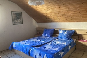 A bedroom with a sloped ceiling, a bed with a blue patterned bedspread, a nightstand, and a wall-mounted picture. - Holiday apartment with 1 bedroom (Bodolz)