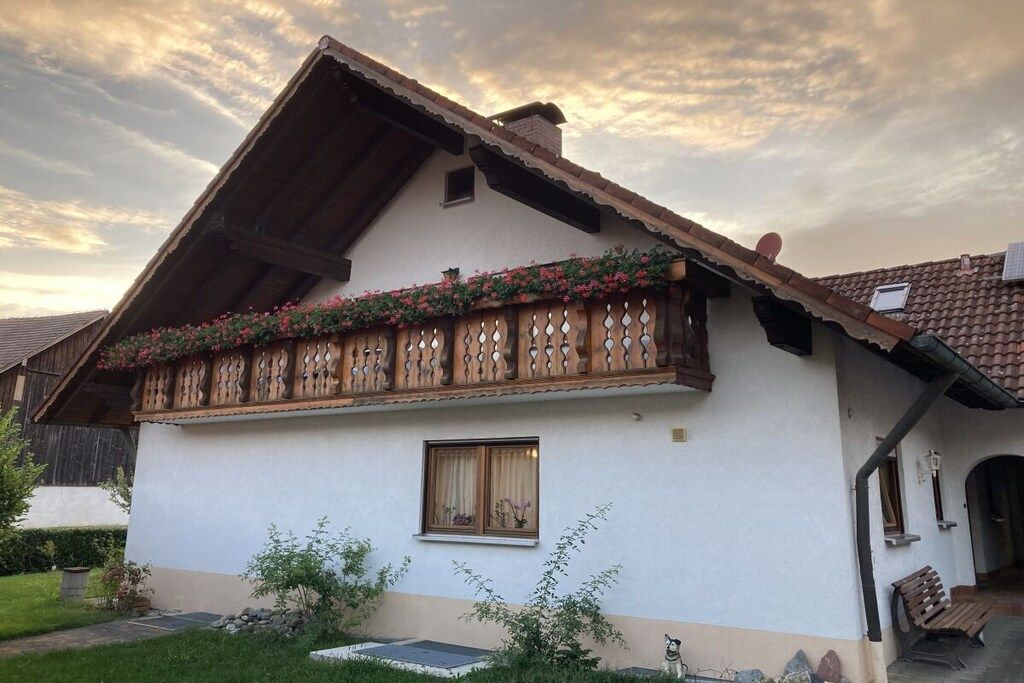 Un chalet traditionnel doté d’un toit à pente, d’un balcon en bois orné de jardinières et d’une petite fenêtre.