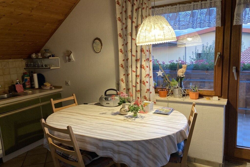 Een eetruimte met een ronde tafel, stoelen, een radio en potplanten.