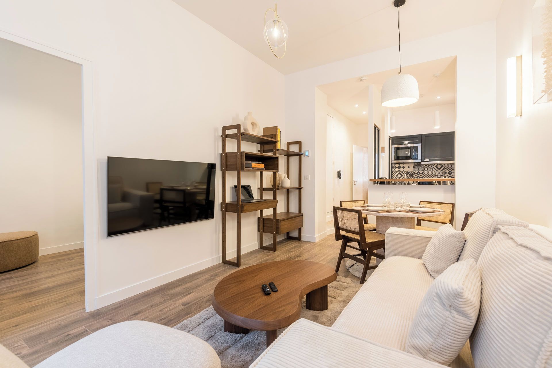 Un salón moderno con un televisor de pantalla plana, una estantería de madera, una mesa de centro redonda y un sofá.