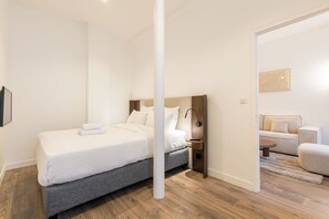 A modern bedroom with a bed, bedside table, and a view into another room. - Elégant appartement près du Moulin Rouge (Paris)