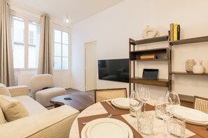 A modern living room with a sofa, a dining table set for two, and a TV mounted on the wall. - Elégant appartement près du Moulin Rouge (Paris)