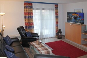 A living room with a sofa, a coffee table, a television, and a red carpet. - Holiday home in Allgäu with 1 bedroom (Lechbruck)