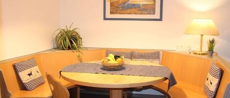 A dining area with a round table, checkered cushions, and a bowl of fruit.