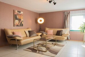 Ein Wohnzimmer mit einem beigefarbenen Sofa, einem Glastisch, einer Stehlampe und einem Bild an der Wand.