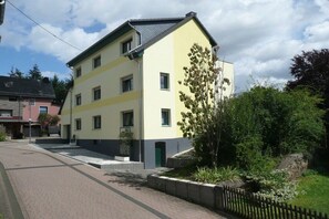 Ein mehrgeschossiges Wohngebäude mit Flachdach, befestigter Auffahrt und kleinem Garten mit Baum und Sträuchern.