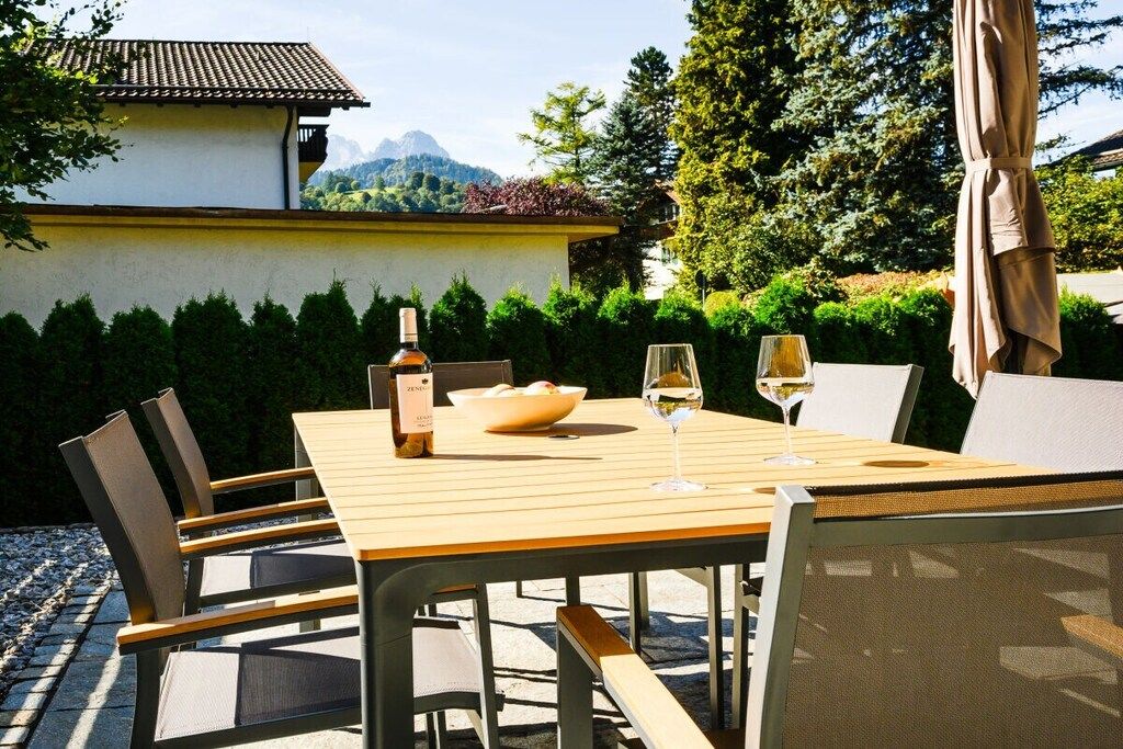 Ein Essbereich im Freien mit Tisch, Stühlen, einer Flasche und Gläsern.