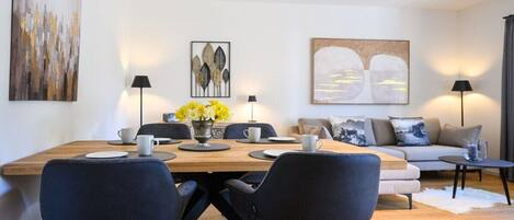 A modern living room with a dining area, featuring a sofa, chairs, a coffee table, and artwork on the walls.