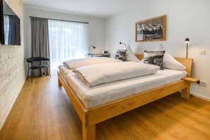 A bedroom with a wooden bed, a desk, a chair, and a window with curtains.