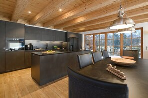 A modern kitchen with a central island, dark cabinetry, and a dining area with a round table and chairs.